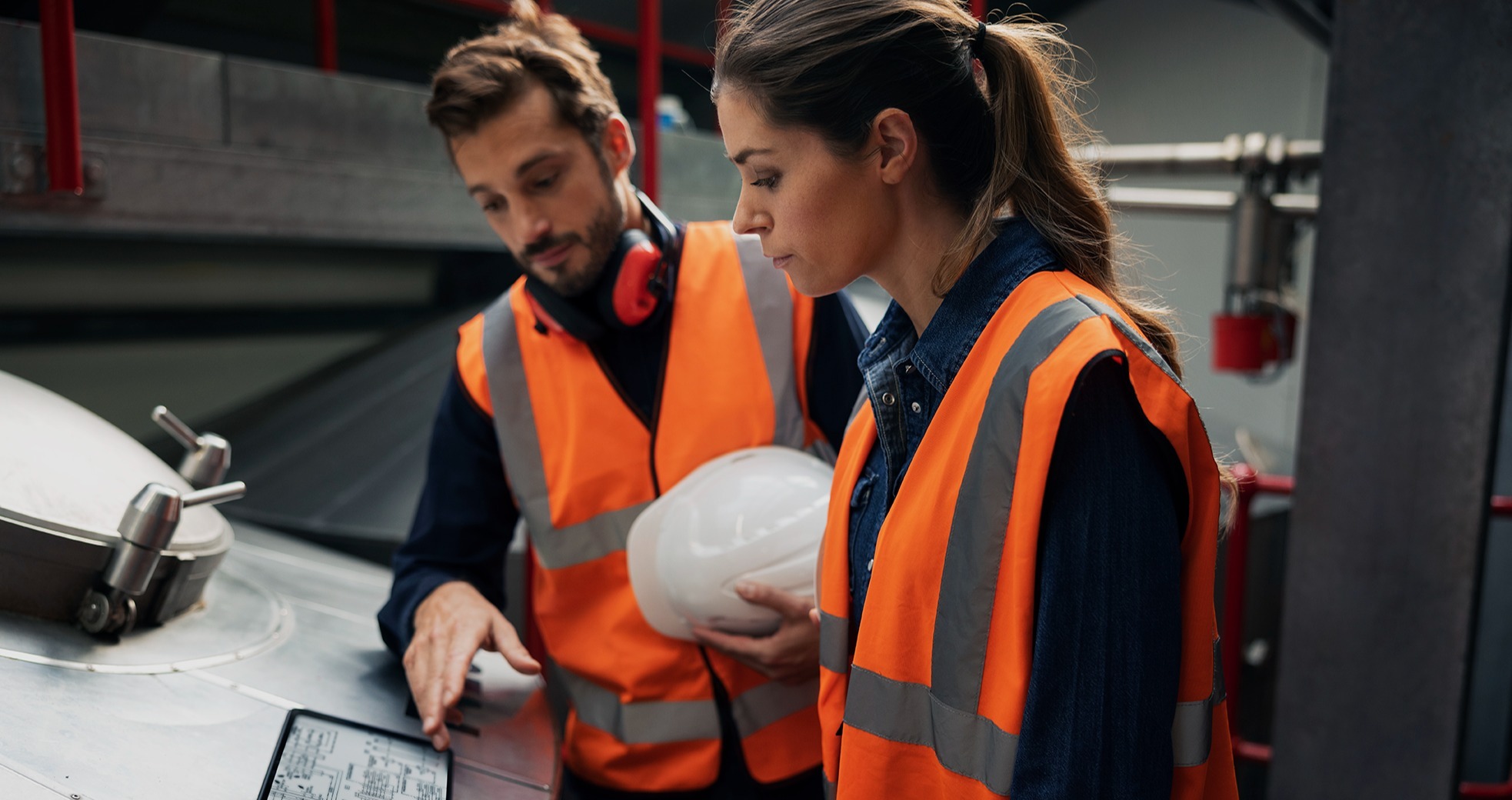 two construction workers in orange vests looking at a tablet